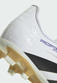 White soccer cleat with textured upper, gold outsole, black accent stripes, and "Predator" branding. Designed for performance on grass.