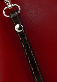 Zwarte leren band met bruine stiksels en een zilveren drukknop bevestigd aan een rood oppervlak, met een gladde textuur en contrasterende kleuren.