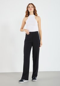 Pantalons noirs à jambes larges avec une texture lisse, associés à un haut sans manches blanc ajusté avec un col montant et un tissu à côtes.