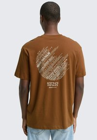 Bruine katoenen t-shirt met een gebogen grafisch ontwerp met witte tekst en coördinaten op de achterkant, korte mouwen en een relaxte pasvorm.