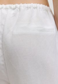 Weiße Leinenhose mit einem elastischen Bund. Eine kleine, horizontale Gesäßtasche ist sichtbar und besteht aus dem gleichen Stoff.