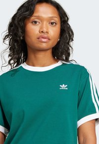 Πράσινο βαμβακερό t-shirt με λευκό γιακά και μανίκια, με τρεις λευκές ρίγες στα πλάγια και ένα μικρό λευκό λογότυπο adidas στο στήθος.
