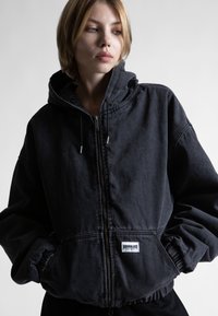 Juodas džinsinis džemperis su gobtuvu, užtrauktuku priekyje, elastingomis rankovėmis ir juosmeniu. Yra balta etiketė kairėje apatinėje pusėje. Minkšta tekstūra.