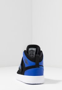 Černé a modré vysoké tenisky s hladkým povrchem, bílou gumovou podrážkou a logem na patě. Uvnitř je viditelná jasná značka.