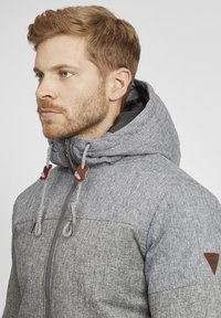Gray fleece jacket with a textured finish, two-tone design, adjustable drawstrings, and leather accents on the hood and chest area.