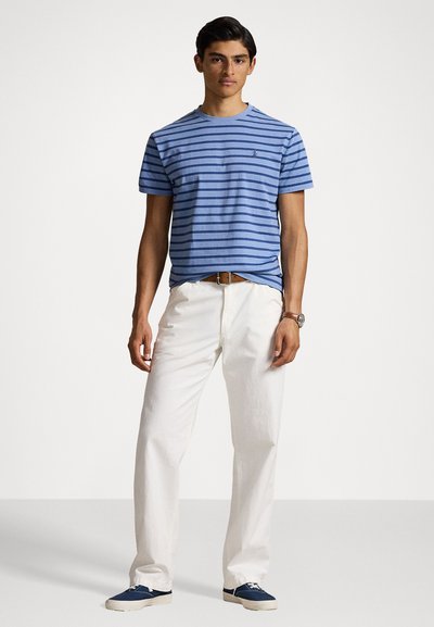 Tricou cu dungi albastre și albe, făcut din bumbac, asociat cu pantaloni albi. Ținuta este completată de încălțăminte bleumarin și o curea maro.