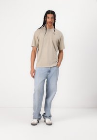 Beige kortærmet t-shirt kombineret med lyseblå jeans, der har en afslappet pasform, ensartet design og subtil tekstur. Casual sneakers.