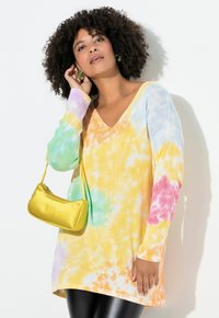 Langärmliges Batik-Oberteil in Pastellfarben (Gelb, Grün, Blau, Rosa) mit V-Ausschnitt. Kombiniert mit einer kleinen gelben Handtasche.