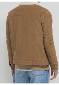 Bruine corduroy jas met witte schapenvachtkraag, geribbelde textuur, nauwsluitend ontwerp en elastische zoom, gezien vanaf de achterkant.