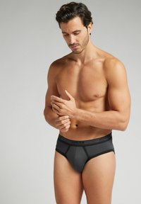 Zwarte slip met elastische tailleband waarop de merknaam staat. Gemaakt van een gladde stof, het heeft contrasterende naden en een aansluitend ontwerp.