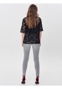 Schwarzes Spitzenoberteil mit kurzen Ärmeln, kombiniert mit grauen schmalen Jeans und burgunderfarbenen High-Heels, von hinten gesehen.