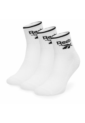 Trzy pary białych skarpetek do kostki z czarną lamówką i logo Reebok na mankiecie, ułożone obok siebie na białym tle.