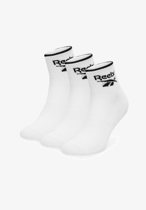 Trzy pary białych skarpetek do kostki z czarną lamówką i logo Reebok na mankiecie, ułożone obok siebie na białym tle.