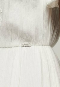 Vestido blanco con una tela texturizada, que presenta una cinturilla y una pequeña etiqueta plateada con la marca "Superdry". Diseño suave y con pliegues.