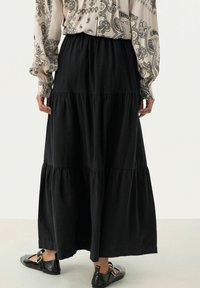 Gonna maxi nera a strati realizzata in tessuto leggero, con una vita elastica e una silhouette fluida. Abbinata a scarpe nere flat.