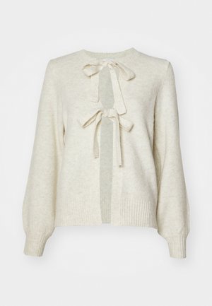 Lys beige genser med rund hals, med to frontsløyfer, ribbede mansjetter og en myk tekstur. Genseren har en åpen frontdesign.