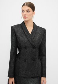 Blazer nero doppiopetto in tessuto testurizzato, con arricciature laterali e grandi bottoni neri. Collo a scollo e vestibilità sartoriale.