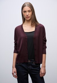 Cardigan a maglia borgogna con scollo a V, chiusura a bottoni e polsini a coste, indossato sopra una maglietta nera e jeans scuri. Design semplice e senza decorazioni.