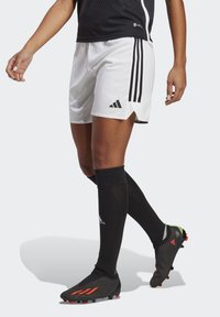 Schwarzes Mesh-Trikot, weiße Shorts mit schwarzen Streifen, schwarze Socken und schwarze Fußballschuhe mit orangen Akzenten.