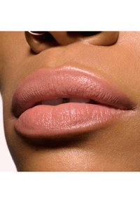 Primo piano di labbra che mostrano un rossetto nude opaco, con una texture liscia e una leggera lucentezza. Il tono della pelle è caldo con sottotoni naturali.