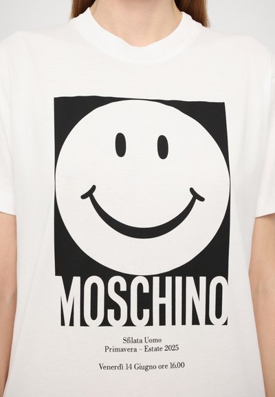 Bílý bavlněný tričko s velkým černým smajlíkem a nápisem "MOSCHINO" pod ním, doplněný o detaily události v černém písmu.