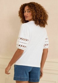 Witte korte mouwen top met poefmouwen en kantdetails. Gecombineerd met denim shorts, die een relaxte pasvorm en een zachte textuur laten zien.
