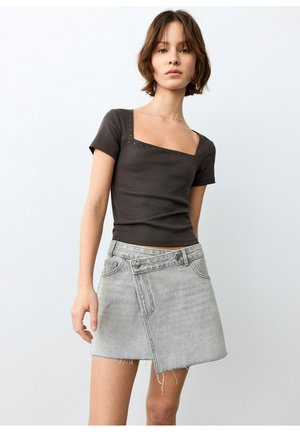 Tânără purtând un top negru cu decolteu pătrat și mâneci scurte, și o fustă mini asimetrică din denim gri deschis, cu tiv franjurat.