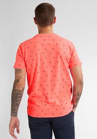 Korallefarbenes T-Shirt mit kurzen Ärmeln und schwarzen Mustern kleiner Figuren, Rundhalsausschnitt, strukturierter Stoff und gerade geschnitten.