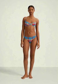 Fargerik bikinitruse med et rutemønster i blått, rødt og gult. Toppen har bøyle og tynne justerbare stropper; bunnen har en lav midje.