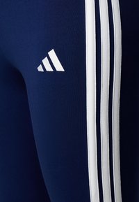 Námornícky športové legíny vyrobené z elastického materiálu majú po stranách biely trojpruhový dizajn a biele logo Adidas na stehne.
