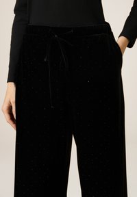 Zwarte fluwelen broek met een zachte textuur, voorzien van een koord in de taille en subtiele stippenaccenten door het geheel. Zakjes aan beide zijden.