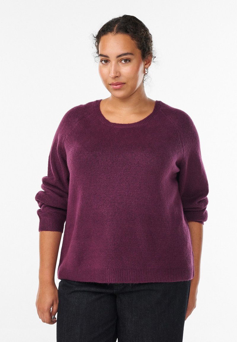 Śliwkowy sweter z okrągłym dekoltem, rękawami raglanowymi i ściągaczami. Miękka tekstura, luźny krój, zestawiony z ciemnymi dżinsami.