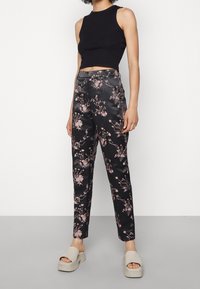 Sorte satinbukser med blomsterdesign i pink, hvid og grøn. Matches med en tætsiddende sort crop top og beige plateausandaler.