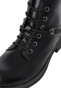 Czarny skórzany botek za kostkę z zaokrąglonym noskiem, wyposażony w sznurowanie, metalowe oczka oraz ozdobny pasek z srebrnymi okuciami.
