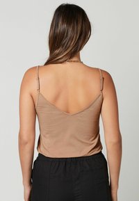 Lichtbruine, aansluitende tanktop met verstelbare spaghettibandjes en een V-vormige achterkant, gecombineerd met broek met elastische taille in het zwart. Zachte textuur.