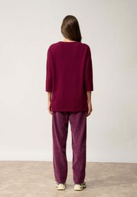 Pull en tricot bordeaux, coupe ample avec des manches trois quarts, associé à un pantalon en velours côtelé assorti. Tissu texturé, silhouette décontractée.