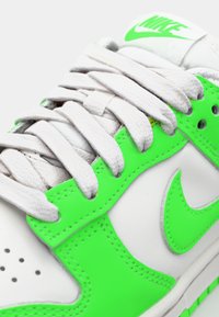 Fehér sneaker neon zöld részletekkel, texturált felülettel, kerek fűzőkkel és hímzett logóval a nyelvén.