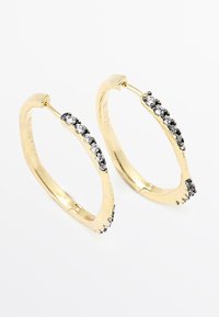 Boucles d'oreilles créoles en or avec un design ondulé, chacune ornée d'une rangée de petits gemstones alternés noirs et blancs.