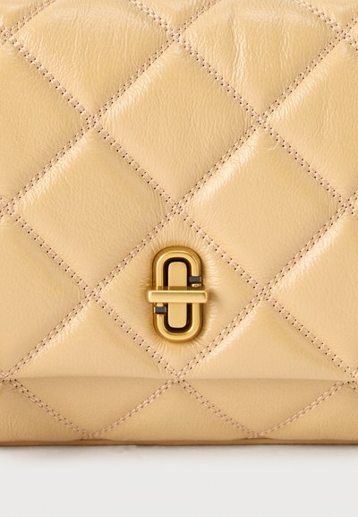 Επιφάνεια από μπεζ καπιτονέ δέρμα με διαμάντι μοτίβο ραφής και κεντρικό χρυσό οβάλ κούμπωμα με οριζόντιο κλειδαριά μπάρα.