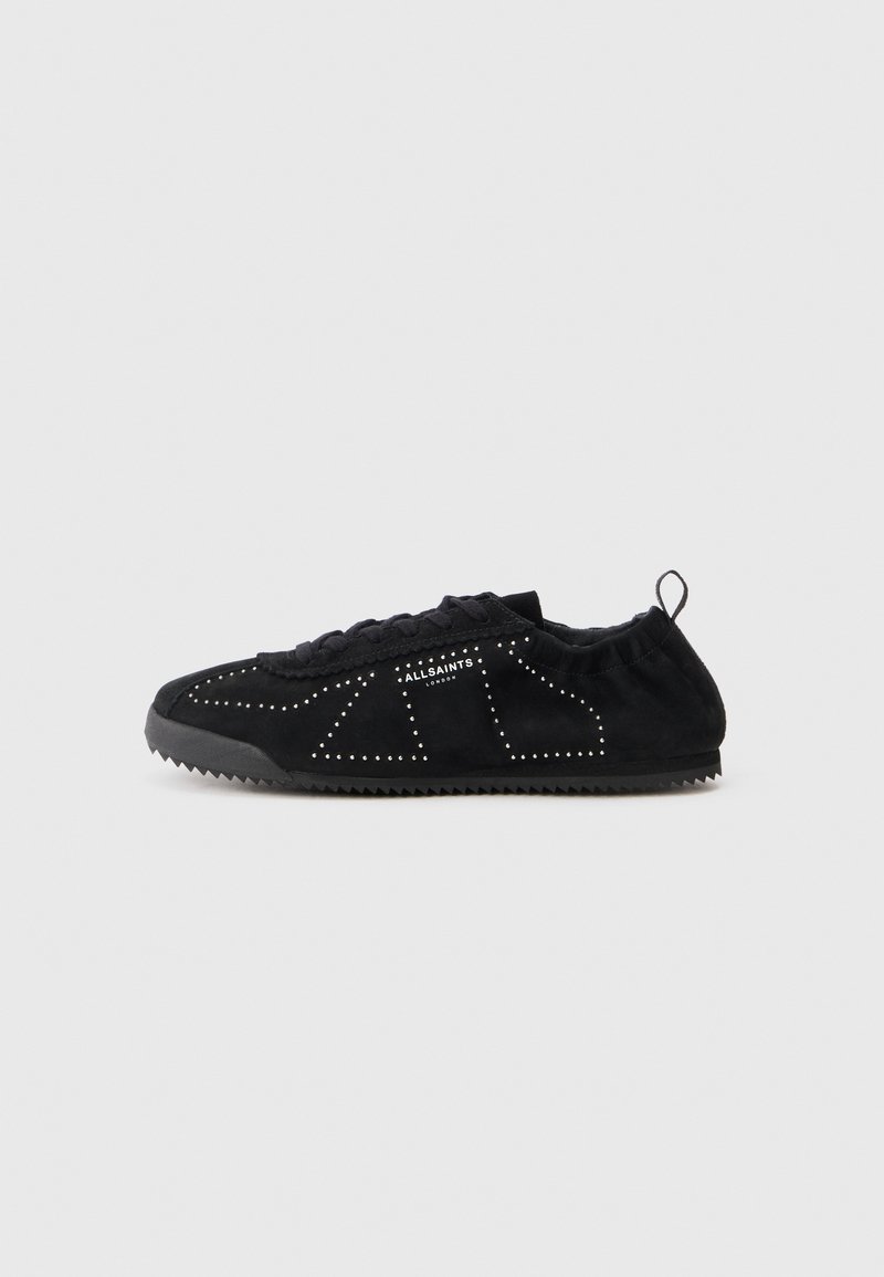 Zapatos de ante negro con punta redondeada, que cuentan con detalles perforados y una suela texturizada para mayor agarre. Incluyen una etiqueta de tela en el talón.