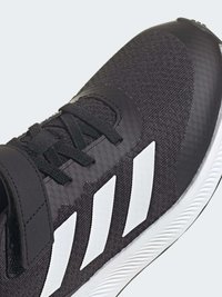 Zapatilla deportiva negra con un upper texturizado, diseño de tres rayas blancas, característica de cordones ajustables y una suela de goma duradera.