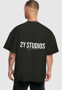 Juoda persiaugusi marškinėlių su trumpomis rankovėmis, ant nugaros raudonai su baltu tekstu "2Y STUDIOS".