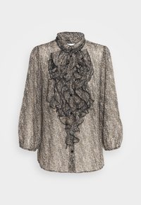 Blusa de patrón en blanco y negro con mangas largas, frente con volantes, cuello alto y cierre de botones, hecha de una tela ligera y texturizada.