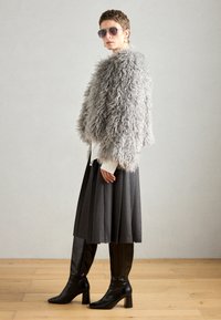 Szara kurtka z sztucznego futra, biała koszulka, plisowana spódnica w kolorze węgla, a także czarne kozaki za kolano na kwadratowych obcasach, dopełnione okularami przeciwsłonecznymi.