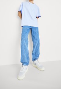 Světle modré oversized tričko, modré rovné džíny a šedobílé tenisky. Jednoduchý design s jemnými detaily šití a volným střihem.