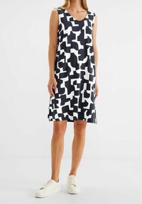 Vestido sin mangas en azul marino y blanco con patrones geométricos abstractos, escote en forma de V y corte holgado, combinado con zapatillas blancas.