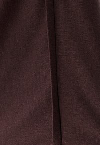 Brunt strikket stof med en struktureret overflade. Har en søm, der løber lodret langs kanten og tilføjer detaljer til designet.