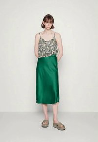 Top de alças com padrão floral em cores claras; saia midi verde em cetim com uma textura suave; sandálias casuais com um design em nós.