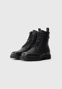 Botas de tobillo de cuero negro con diseño de cordones, ojales dorados, suela de goma resistente y tirador en el talón. Textura suave con mínimos acentos.