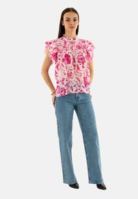 Blusa floral en rosa y blanco con mangas acampanadas, combinada con jeans rectos de mezclilla azul claro y tacones negros de punta.